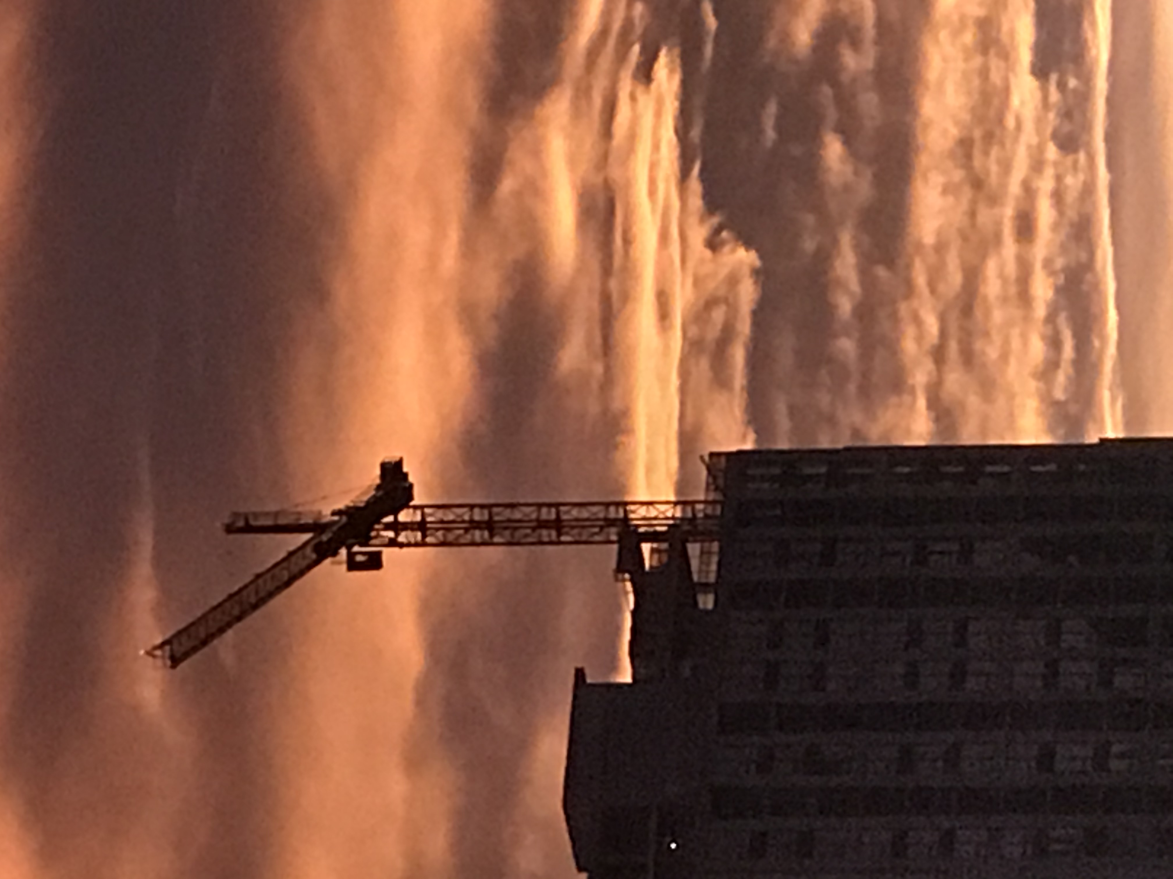 A photograph of golden sky and an unfinished expensive high-rise complex sitting in front on the left with a crane.